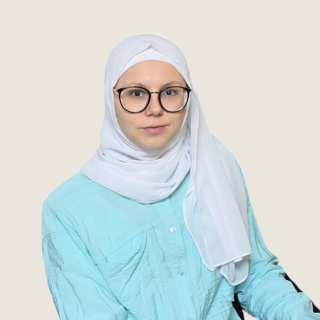 Eine Person mit Brille trägt ein hellblaues Oberteil und einen weißen Hijab.
